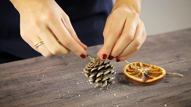 Insérez la corde dans l’oeillet et faites un noeud afin d’immobiliser la pomme de pin.